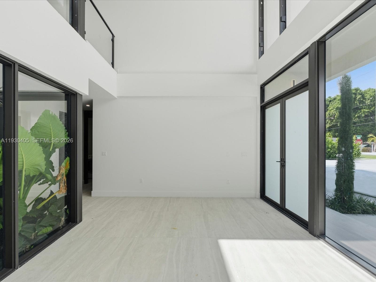 Double-height volume featuring floor-to-ceiling glass windows, full-length stone-finish flooring, metal-framed double glass entry doors, and a glass-paneled mezzanine railing