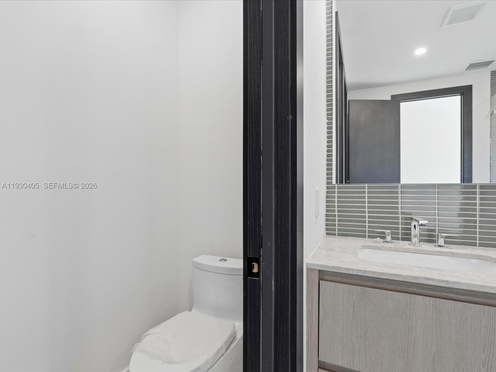 Bathroom featuring a wood-finish vanity, stone-composite countertop with an integrated basin, chrome widespread faucet, and a horizontal-tile backsplash extending to a mirror