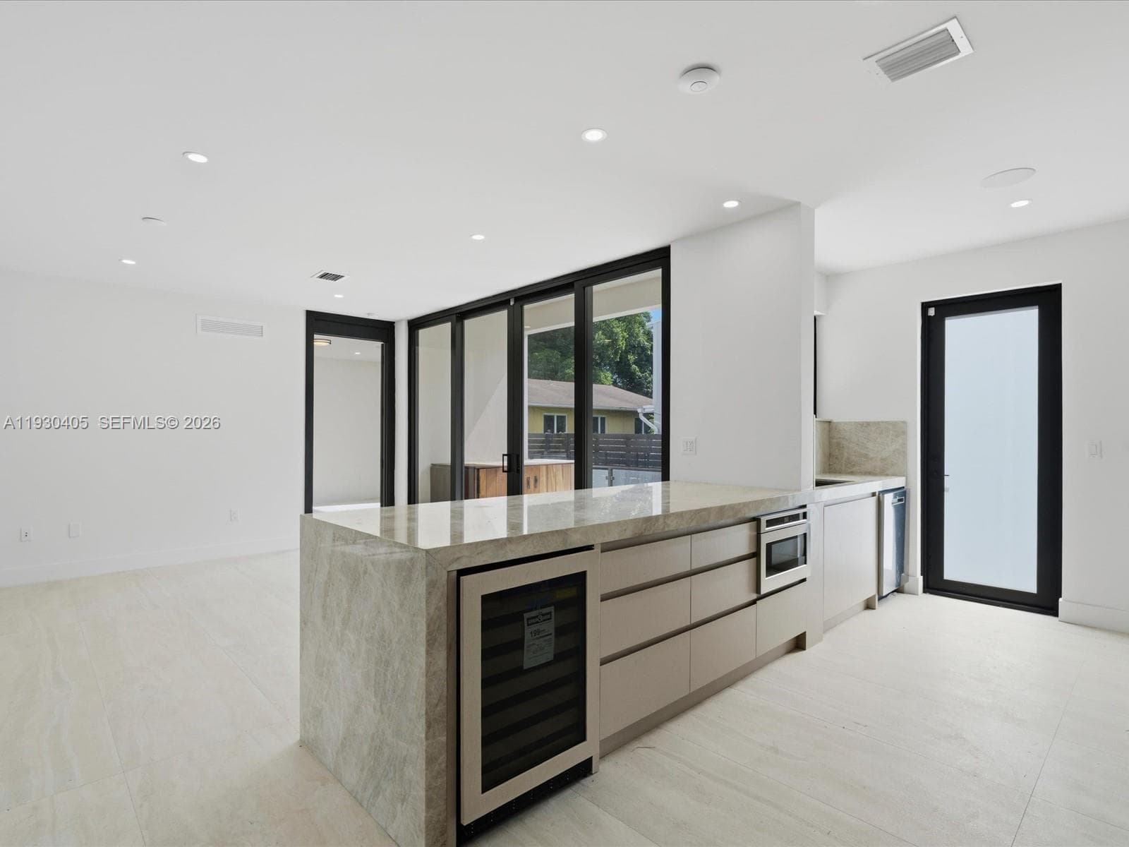 Kitchen featuring an expansive stone-topped island with an integrated wine refrigerator, custom flat-panel cabinetry, recessed lighting, and expansive glass sliding doors