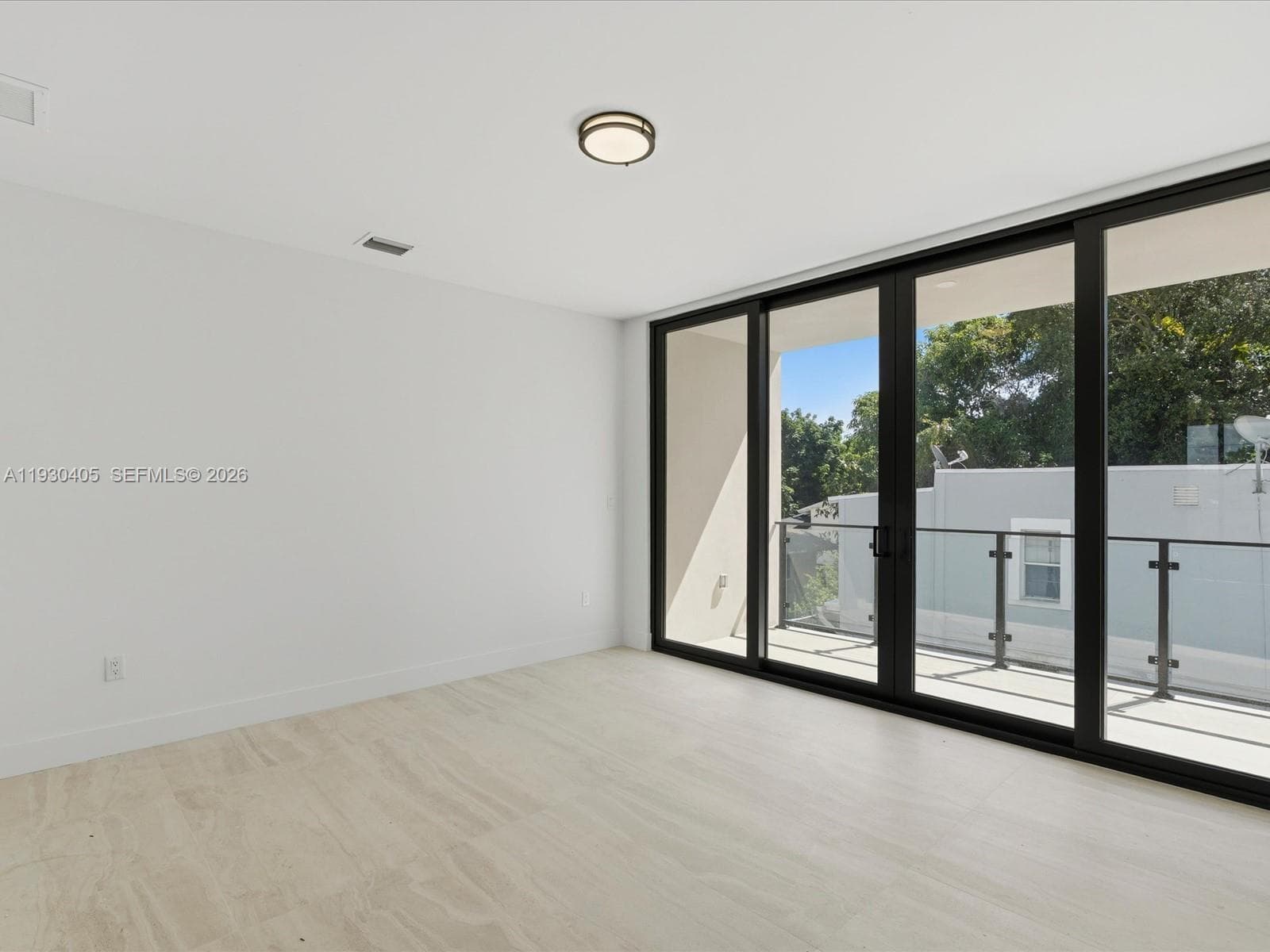 Floor-to-ceiling multi-panel sliding glass doors, neutral stone-finish flooring, recessed ceiling lighting, and a private balcony with glass and metal railings