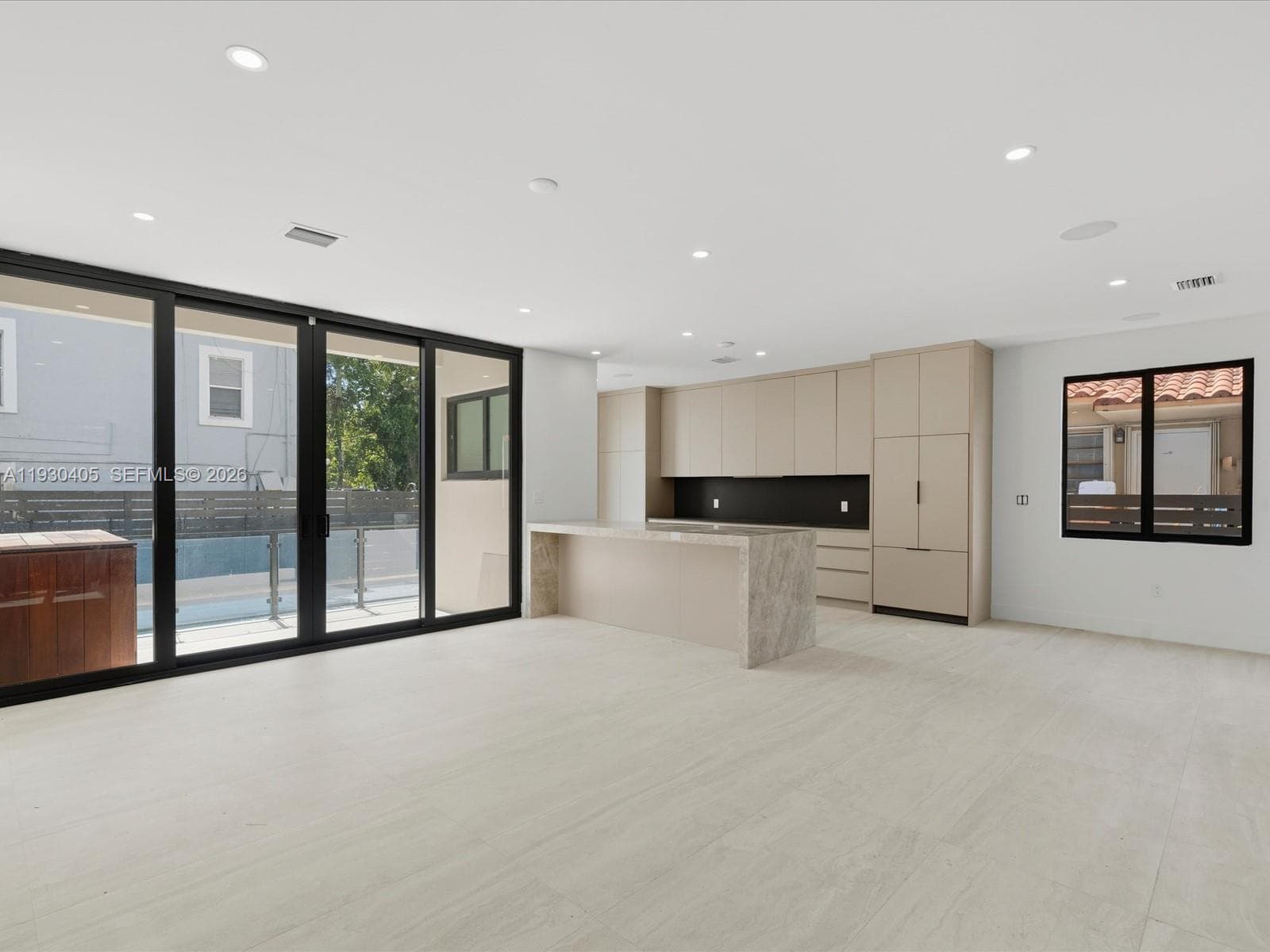 Open-concept interior featuring light-toned flooring, custom flat-panel cabinetry, a stone-finished kitchen island, integrated appliances, and floor-to-ceiling sliding glass doors
