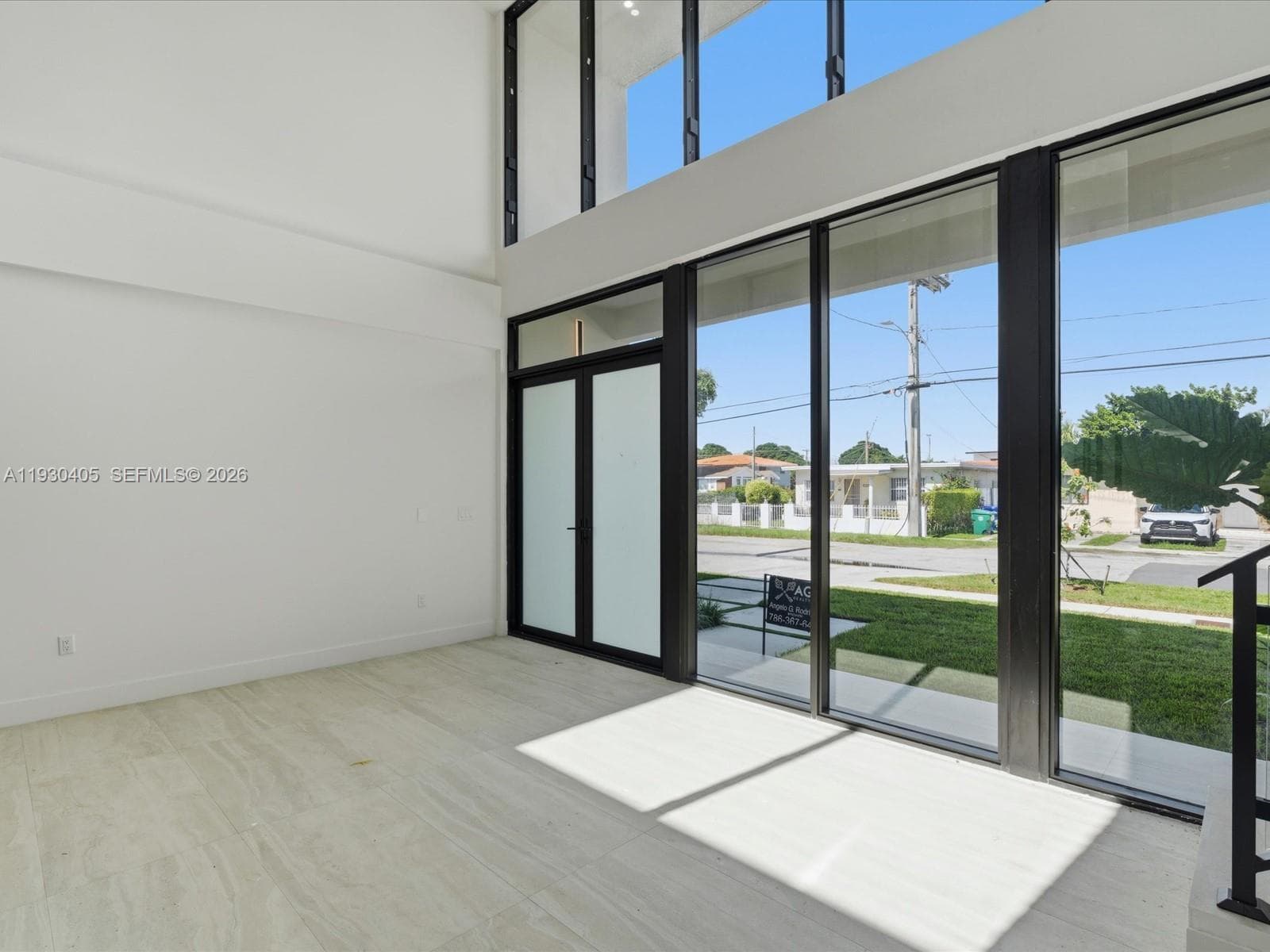 Double-height ceiling, floor-to-ceiling windows with black frames, tile flooring, and frosted glass paneled door