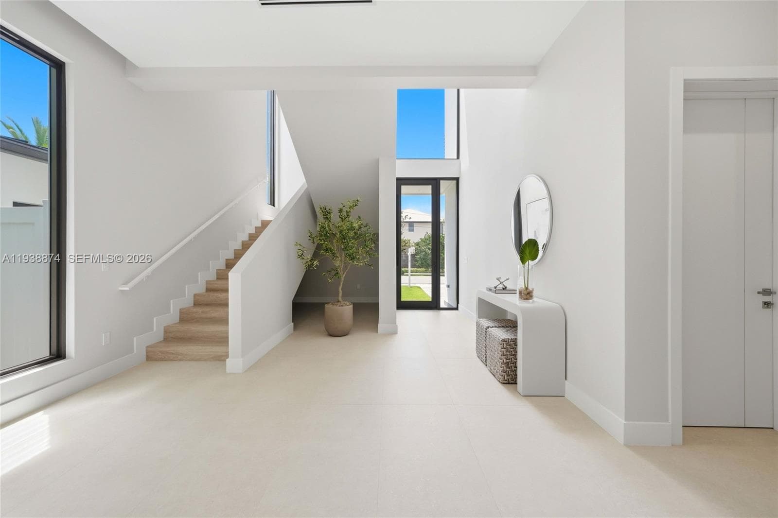 Entry featuring large-format porcelain floors flooring, double-height ceilings, a glass-paneled entry door, full-length windows, and a staircase with wood-finish treads