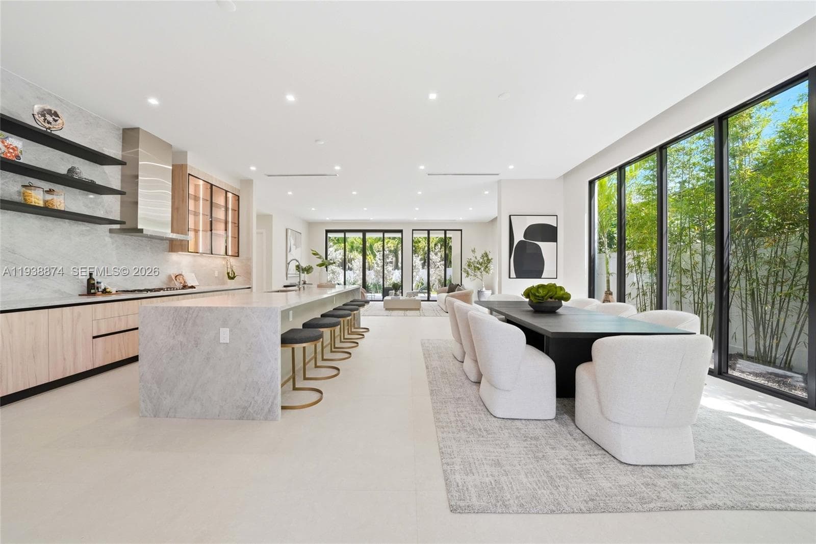 Kitchen featuring a waterfall-edge stone island, light-finish cabinetry, floating shelves, stainless steel range hood, and floor-to-ceiling glass panel windows