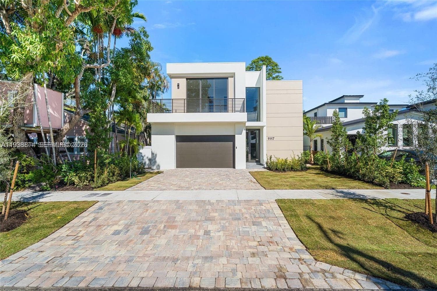 Modern two-story architectural exterior featuring smooth stucco siding, an upper-level balcony with horizontal metal railings, a paver driveway, and an integrated two-car garage