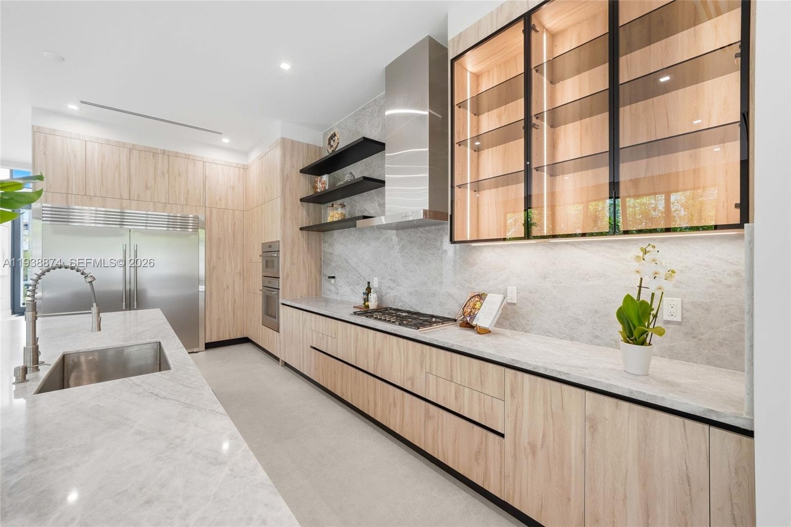 Kitchen featuring light wood-finish cabinetry, stone-style countertops, integrated stainless steel appliances, glass-front upper cabinetry, and open floating shelving