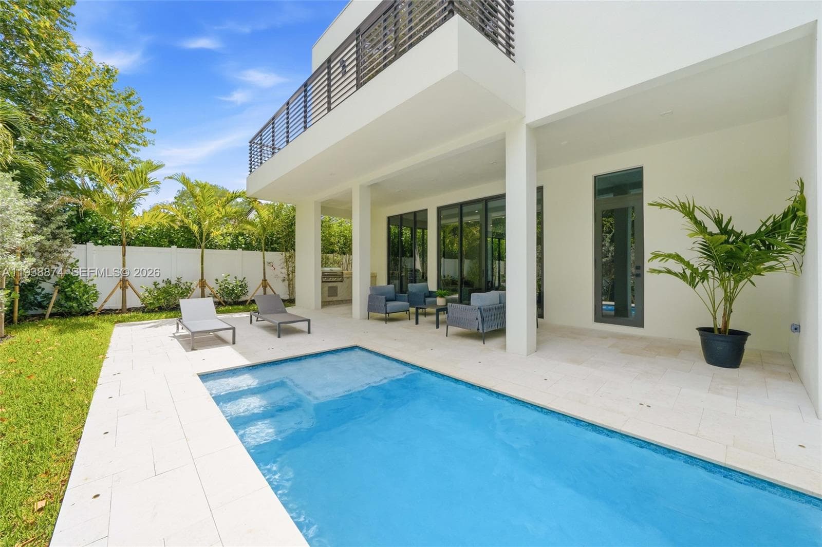 Covered patio with integrated outdoor kitchen, stone-tile pool deck, rectangular swimming pool, and second-story balcony with metal railing