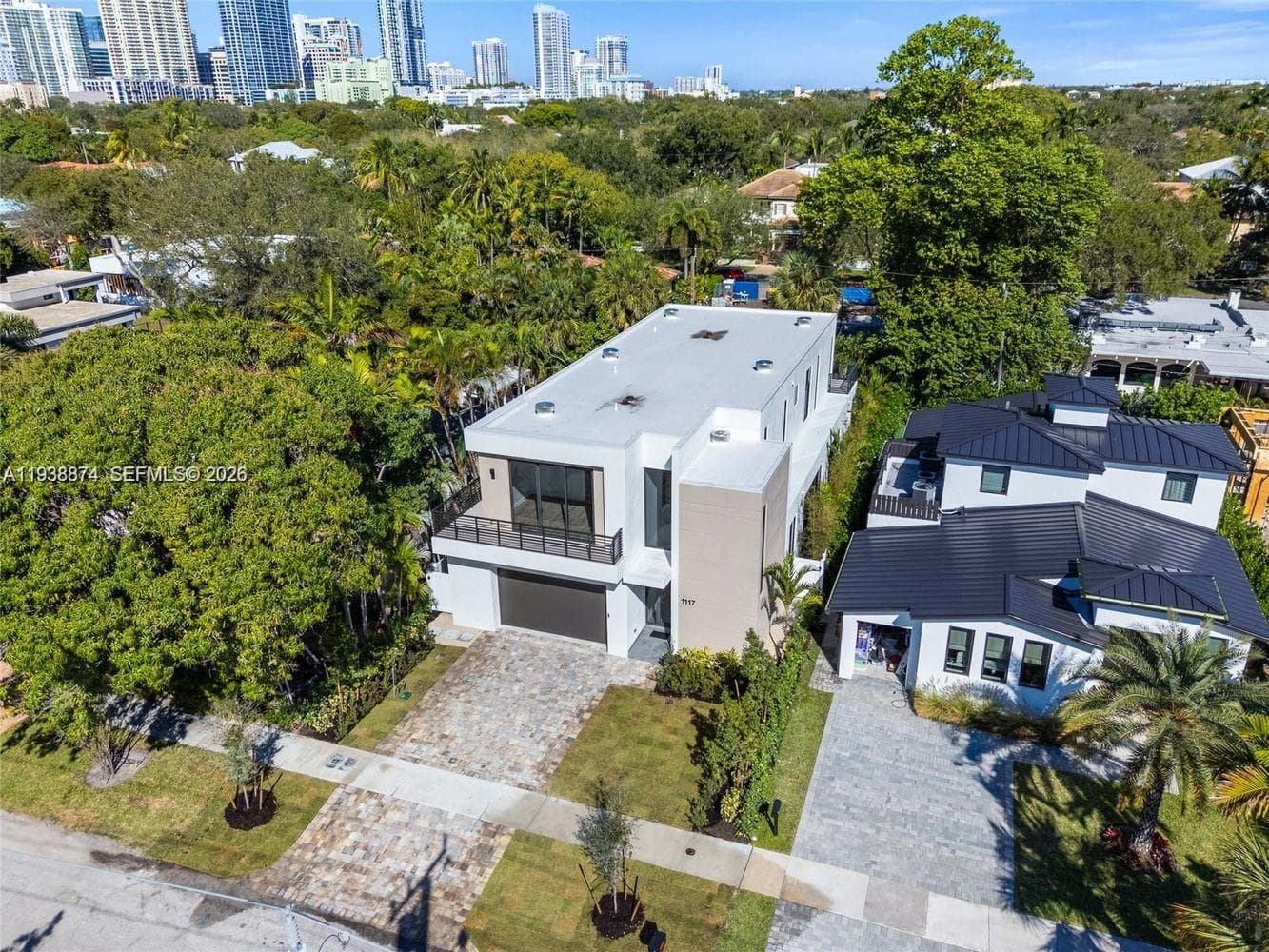Modern two-story structure featuring a flat roof, integrated garage, upper-level terrace with metal railings, and a stone-paved driveway