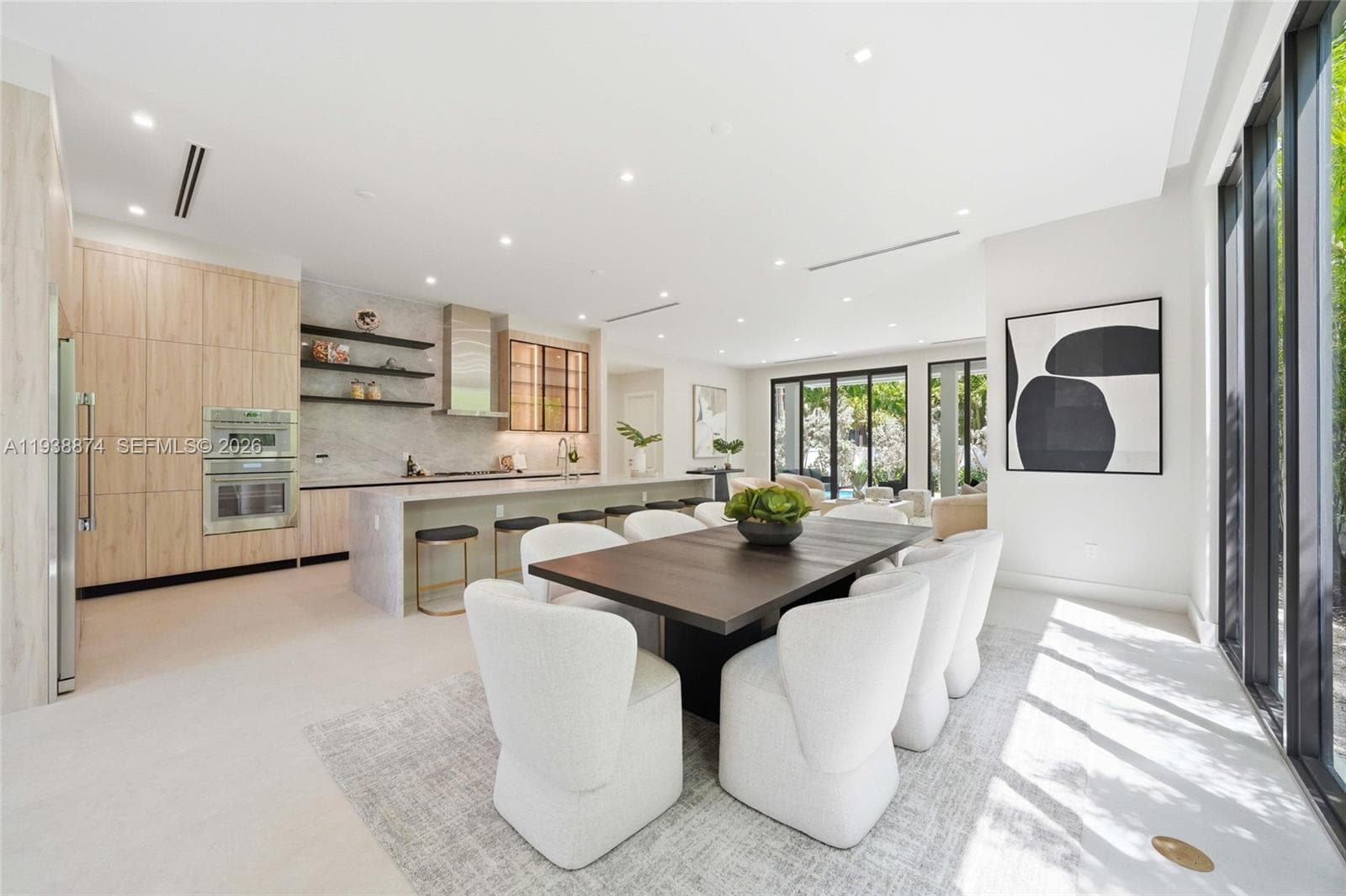 Kitchen featuring floor-to-ceiling wood-finish cabinetry, stone-surfaced waterfall island, built-in stainless steel appliances, floating shelving, and full-height glass panel walls