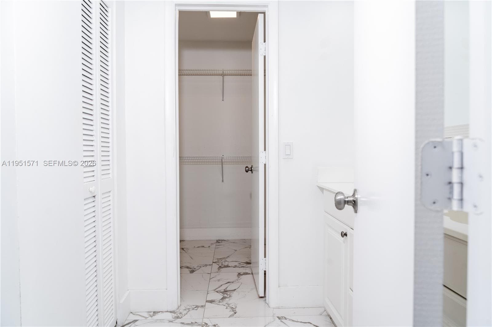 Large-format tile flooring, built-in wire shelving, louvered closet doors, and vanity cabinetry with a solid-surface countertop