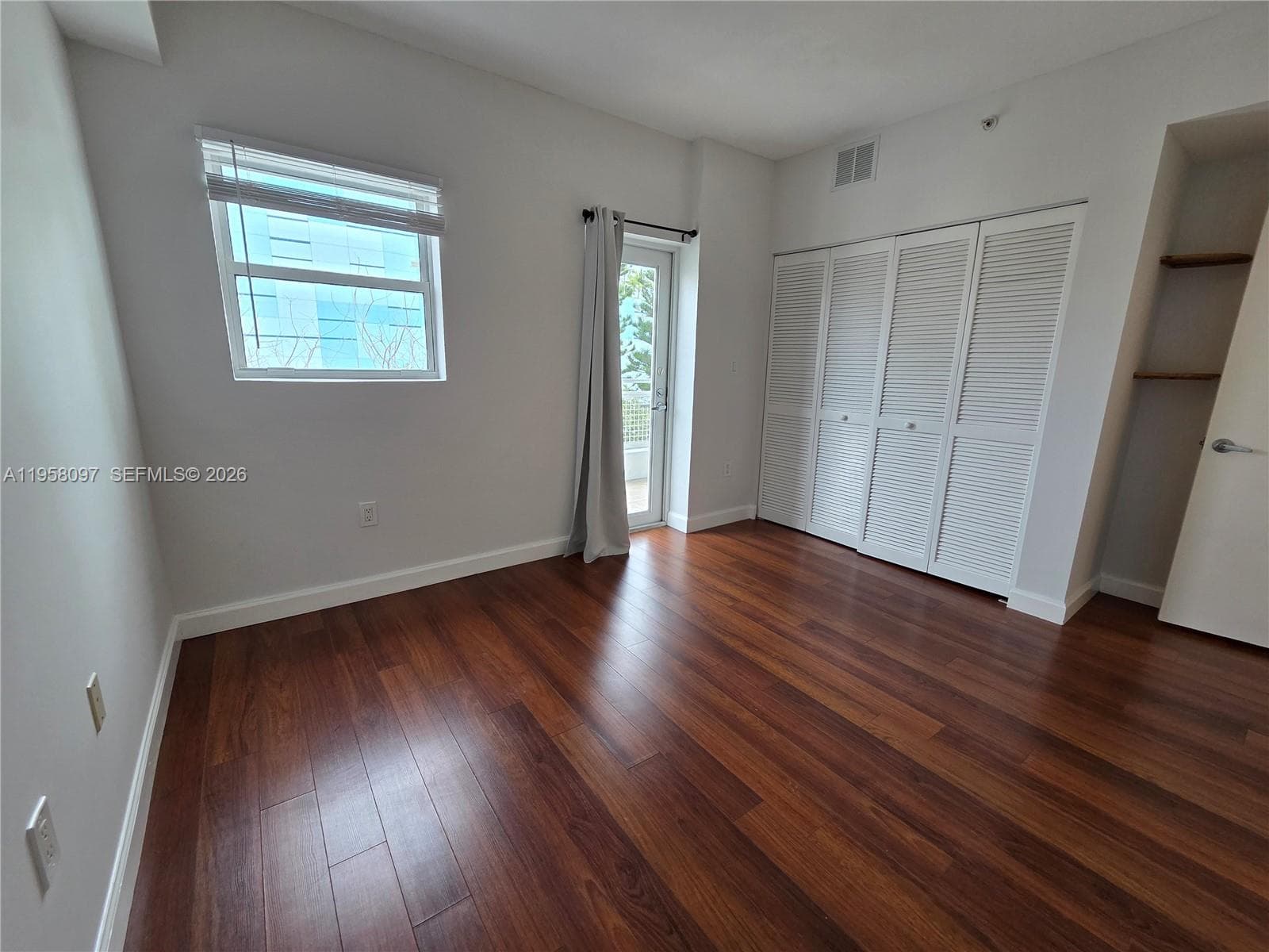 Well-proportioned bedroom featuring double-door closet, clean neutral walls, and warm wood flooring for a modern yet inviting feel.
