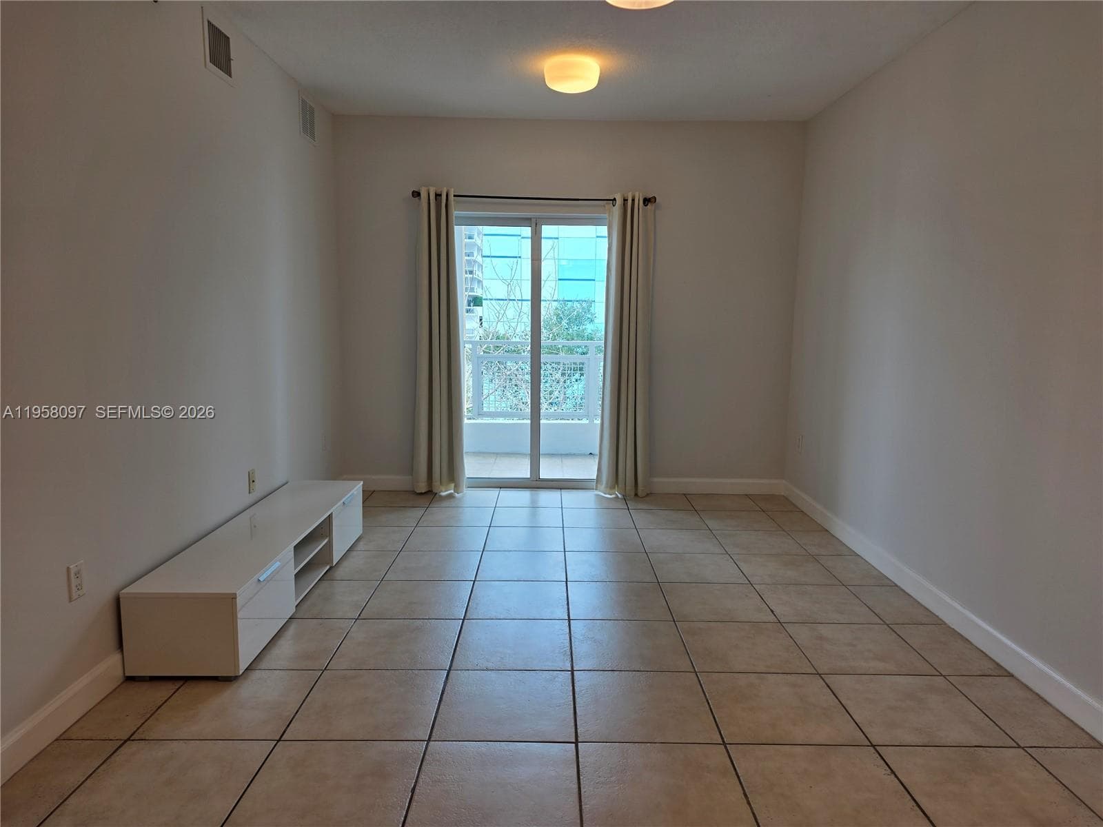 Living room with sliding glass doors leading to a private balcony, offering natural light and city surroundings.