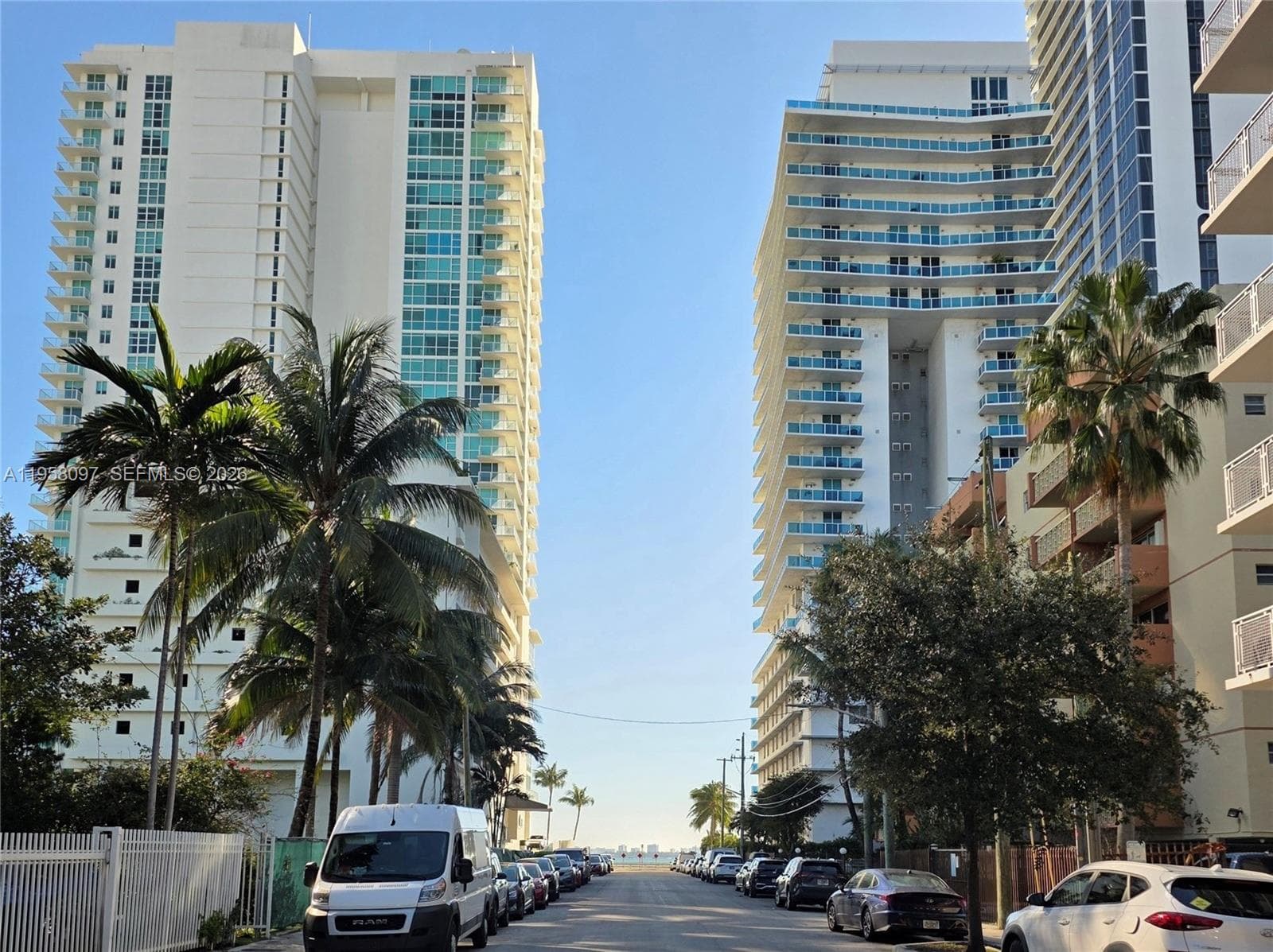 Street-level view of property surrounded by mature palms and neighboring high-rises.