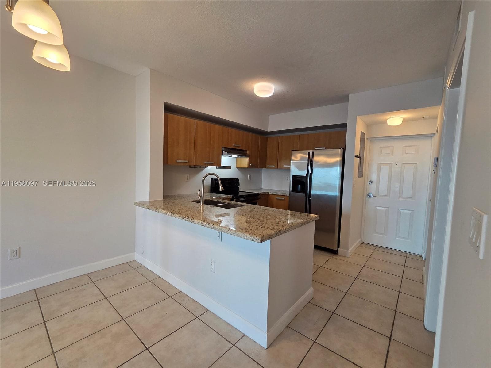 Modern kitchen with granite countertops, wood cabinetry, stainless steel appliances, and breakfast bar overlooking the living space.