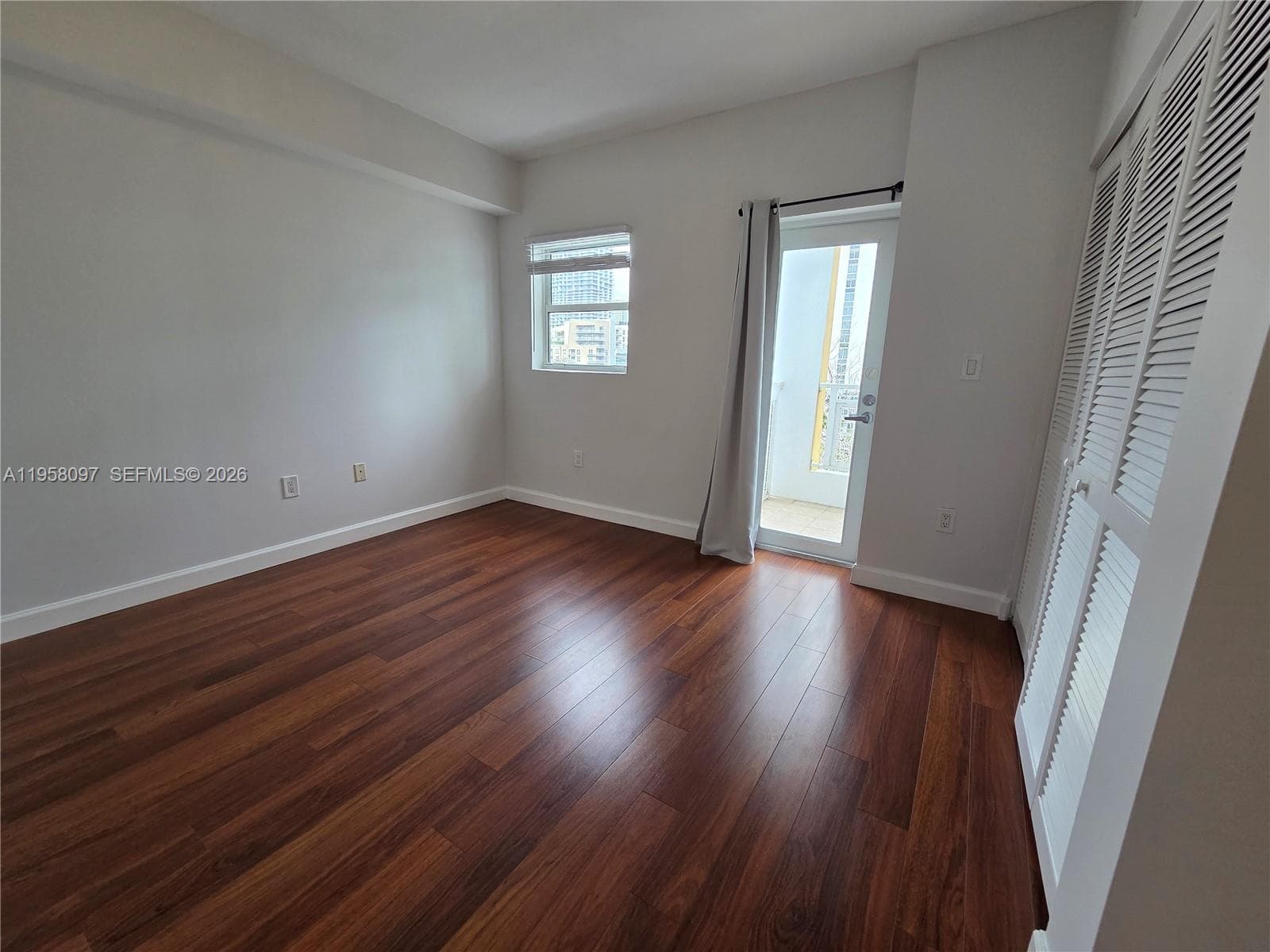Comfortable bedroom with rich wood flooring, generous closet space, and large window allowing for natural light.