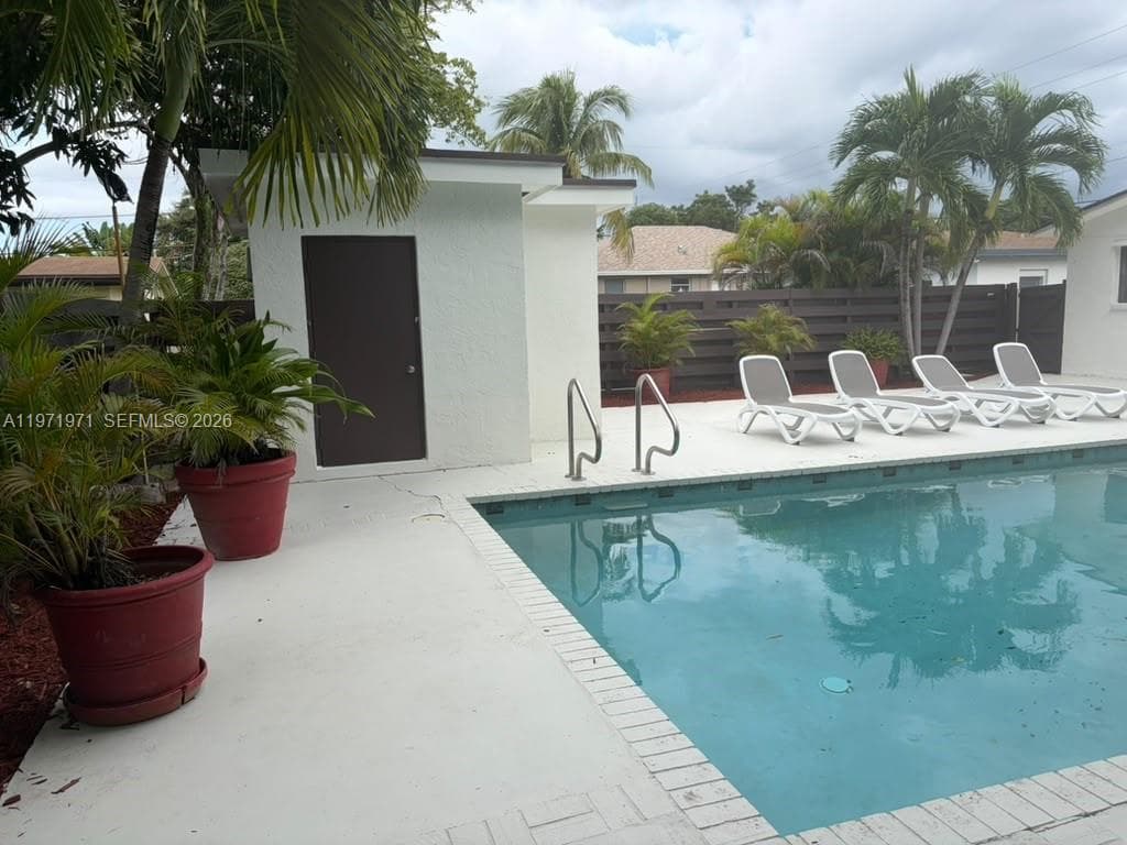 In-ground swimming pool with metal handrails and a concrete pool deck, enclosed by a dark wood-finish privacy fence