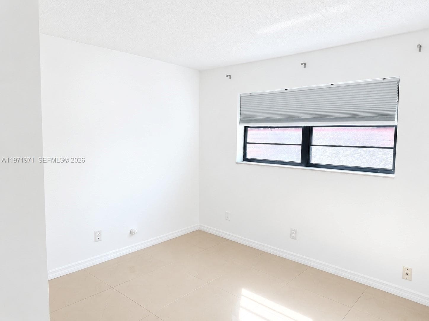 Neutral-toned tile flooring, white wall finish, and a horizontal window featuring a fitted pleated shade