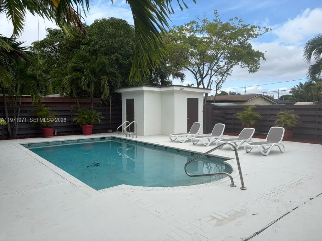 In-ground pool featuring a tile border and metal handrails, surrounded by concrete decking, enclosed by horizontal privacy fencing, and including a detached storage structure