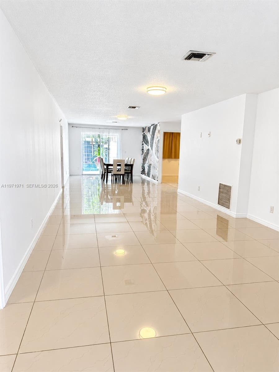 Spacious open-concept interior featuring large-format polished tile flooring, crisp white walls, and sliding glass doors with exterior access