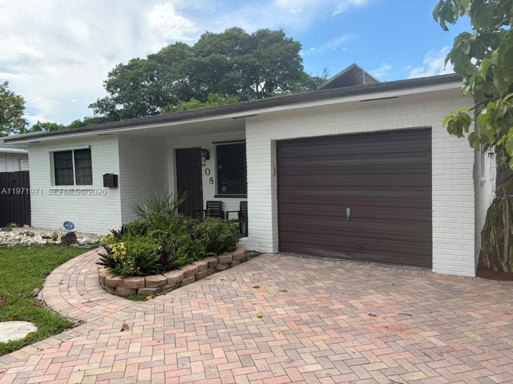 Painted brick exterior featuring a single-car garage, herringbone-patterned paver driveway, integrated stone-walled planter, and covered entryway