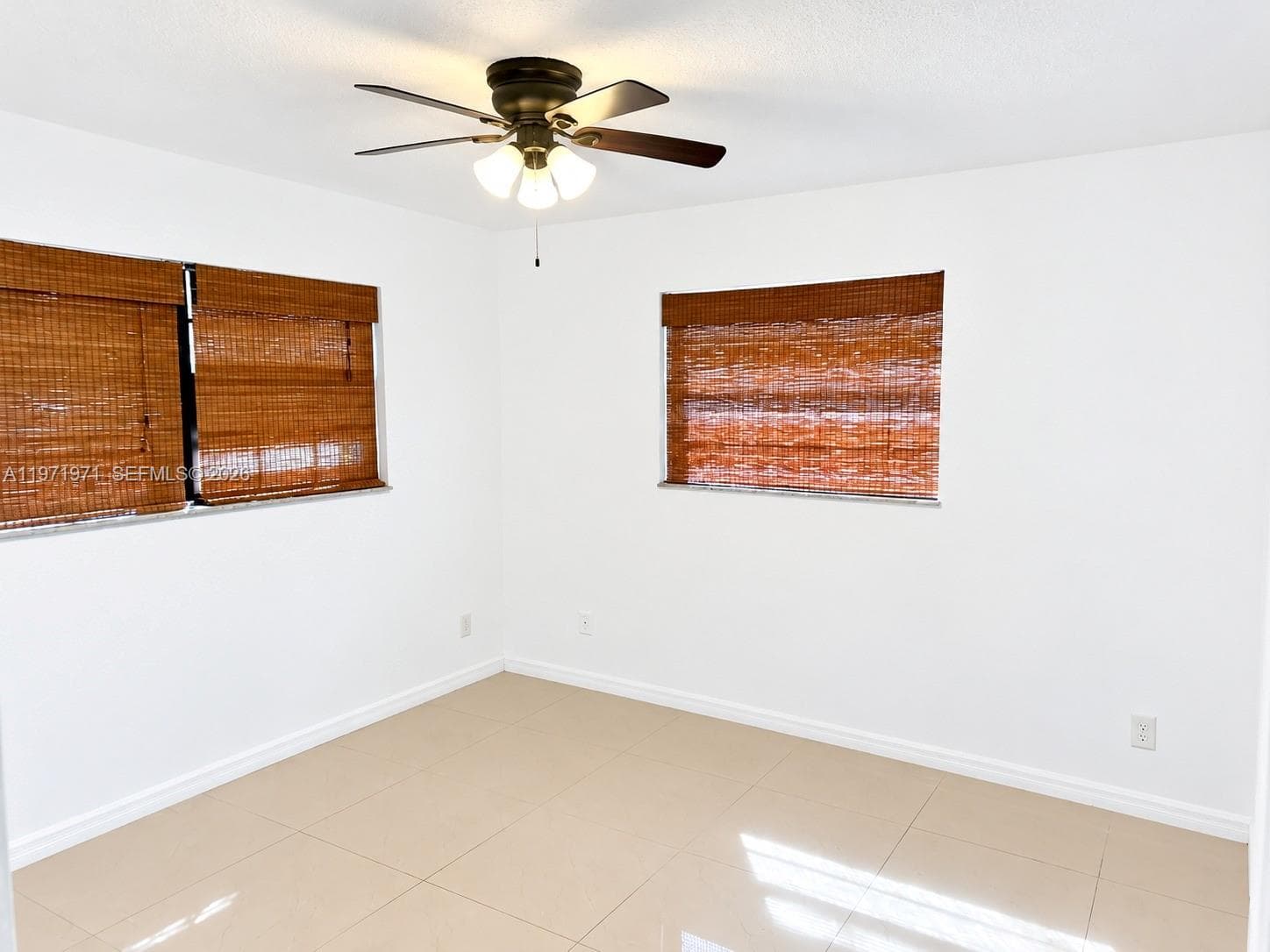 Neutral-toned tiled flooring, wall-mounted ceiling fan with multi-light fixture, and woven bamboo-style window shades