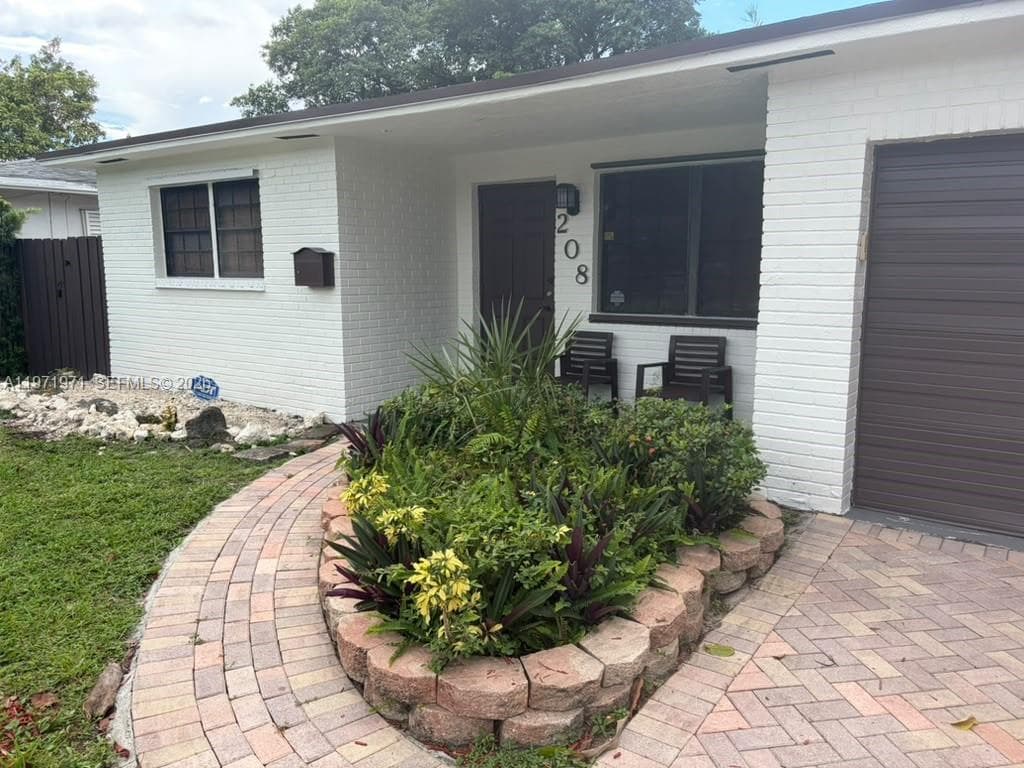 Painted brick exterior featuring a multi-tone paver walkway, curved stone block garden border, attached garage, and metal-framed windows