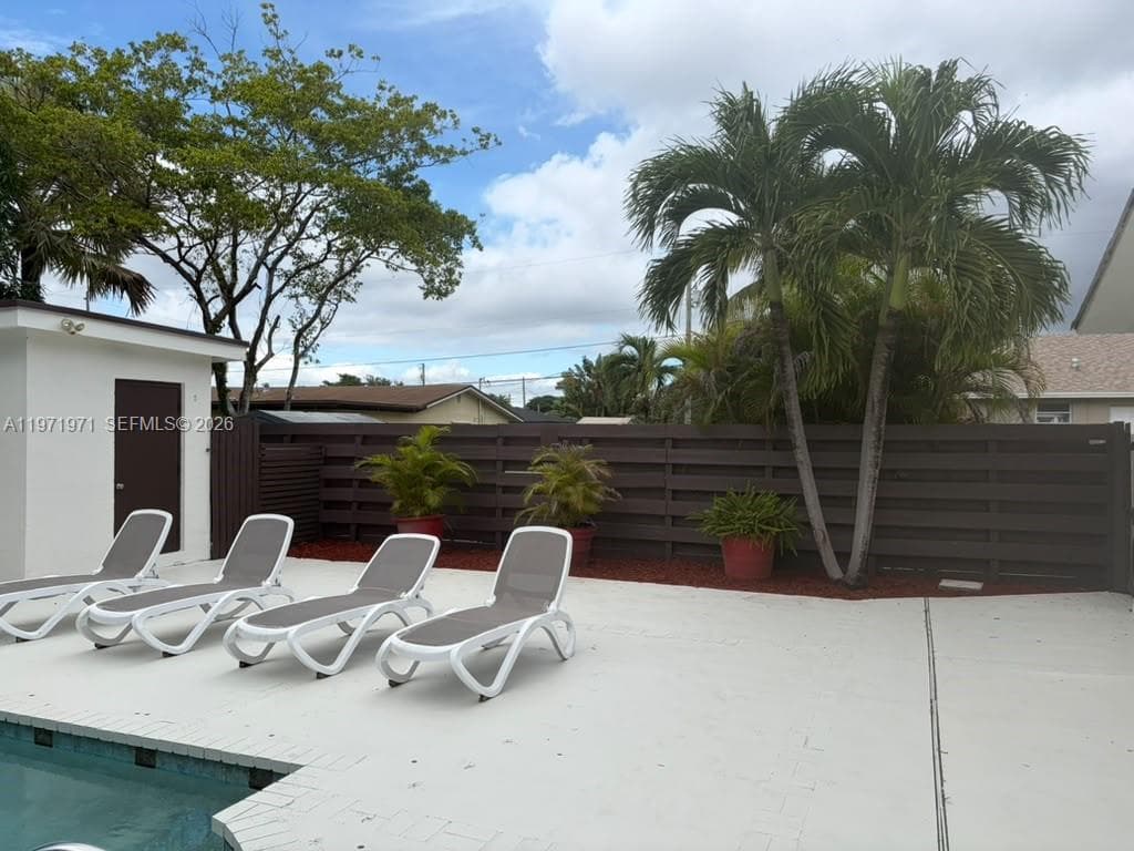 Outdoor space featuring a swimming pool, concrete patio, horizontal slat privacy fencing, and mature palm trees