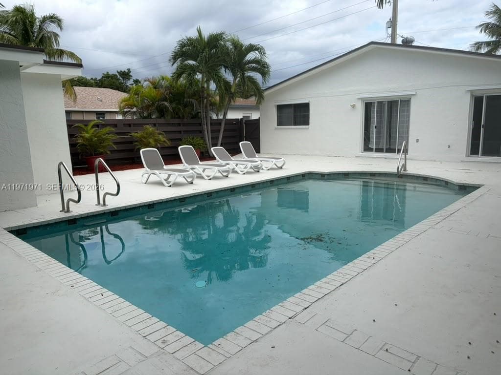 In-ground swimming pool featuring a concrete deck, metal handrails, and a horizontal-slat privacy fence