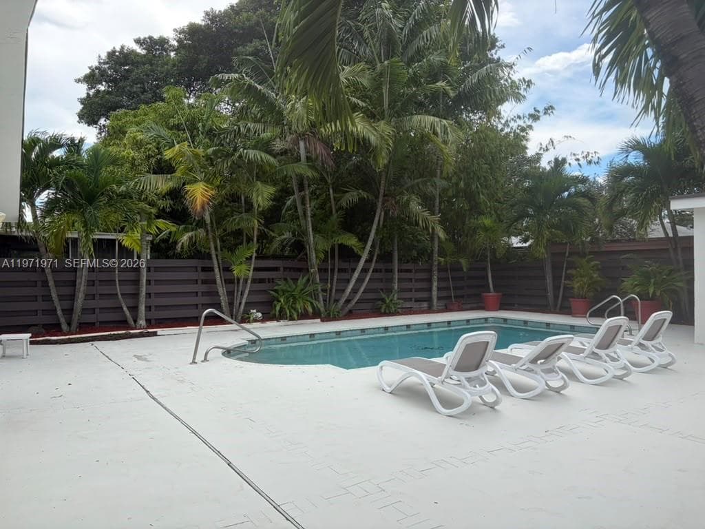 In-ground swimming pool featuring a concrete deck, perimeter palm trees, and horizontal privacy fencing