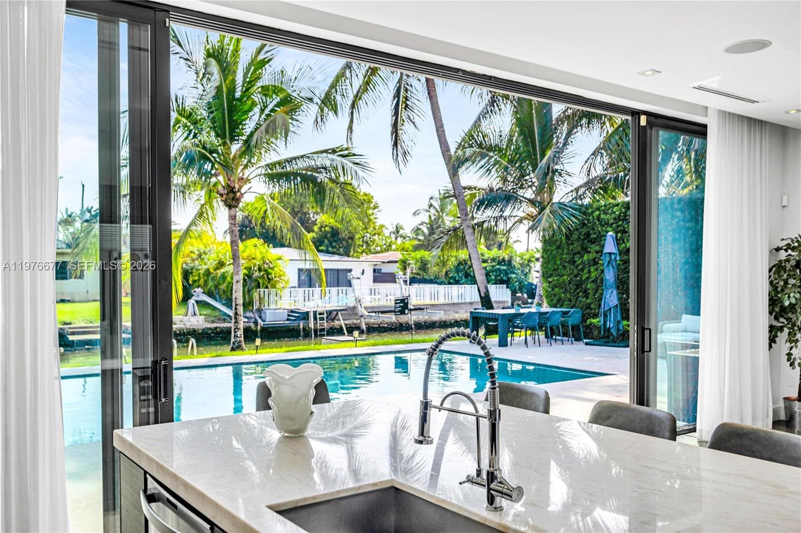 Kitchen island featuring a light-toned countertop, under-mount sink, and high-arch chrome faucet, complemented by wall-to-wall sliding glass doors opening to a pool and canal-front exterior