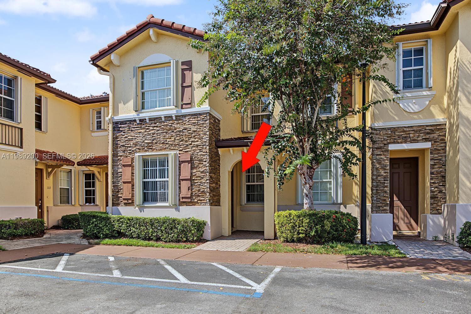 Stucco and stone veneer exterior featuring a recessed entryway, tiled roof, decorative shutters, and manicured shrubbery