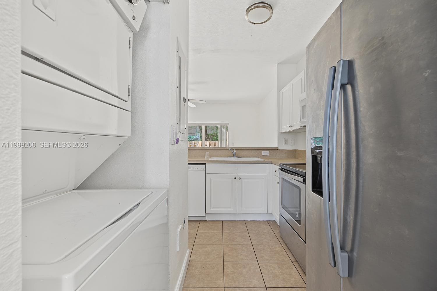 Kitchen featuring white cabinetry, integrated stainless steel appliances, ceramic tile flooring, and dedicated laundry area with stacked washer and dryer