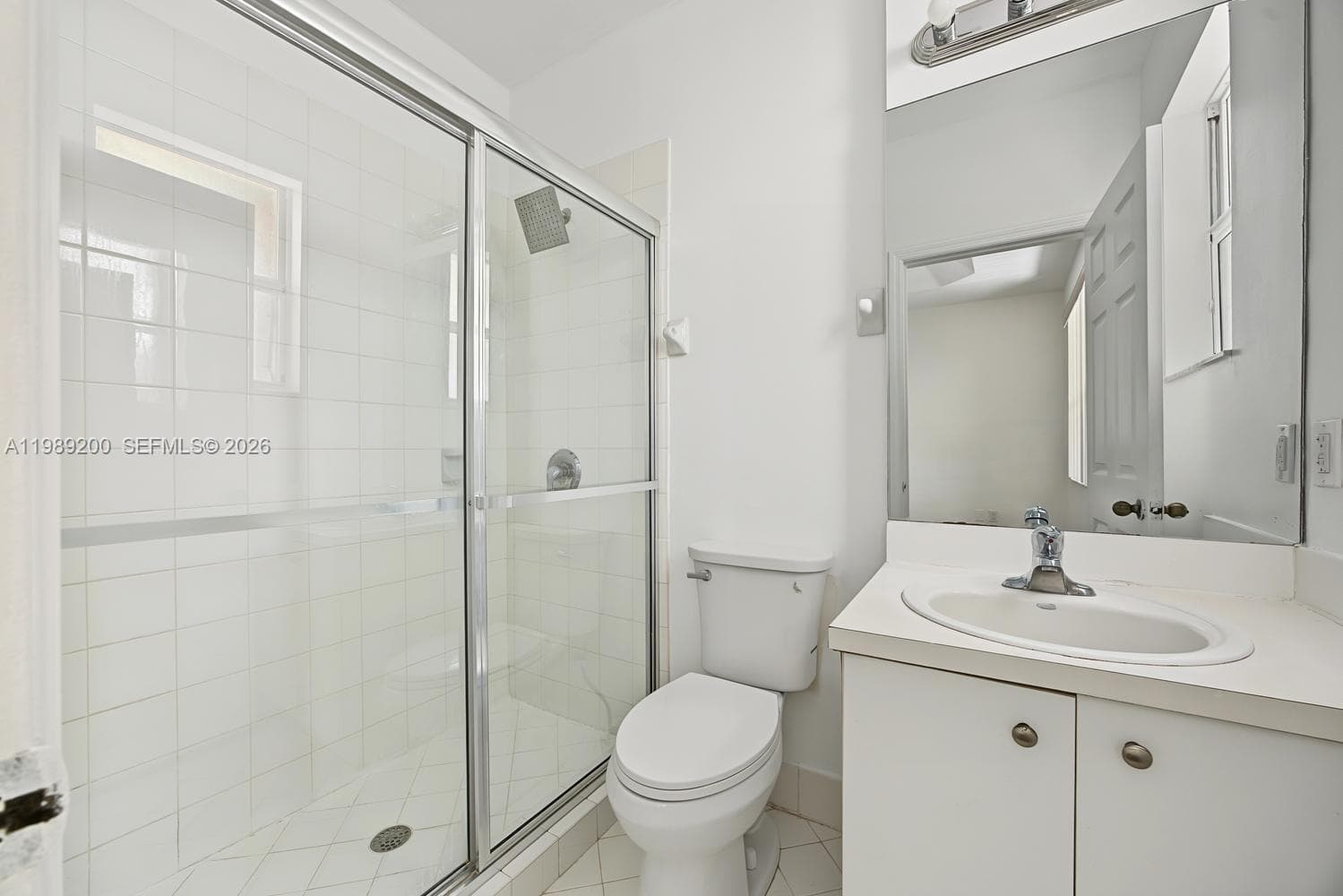 Bathroom featuring a glass-enclosed shower with white wall tile, a white vanity with an integrated basin, a polished chrome faucet, and a wall-mounted vanity mirror with integrated light fixture