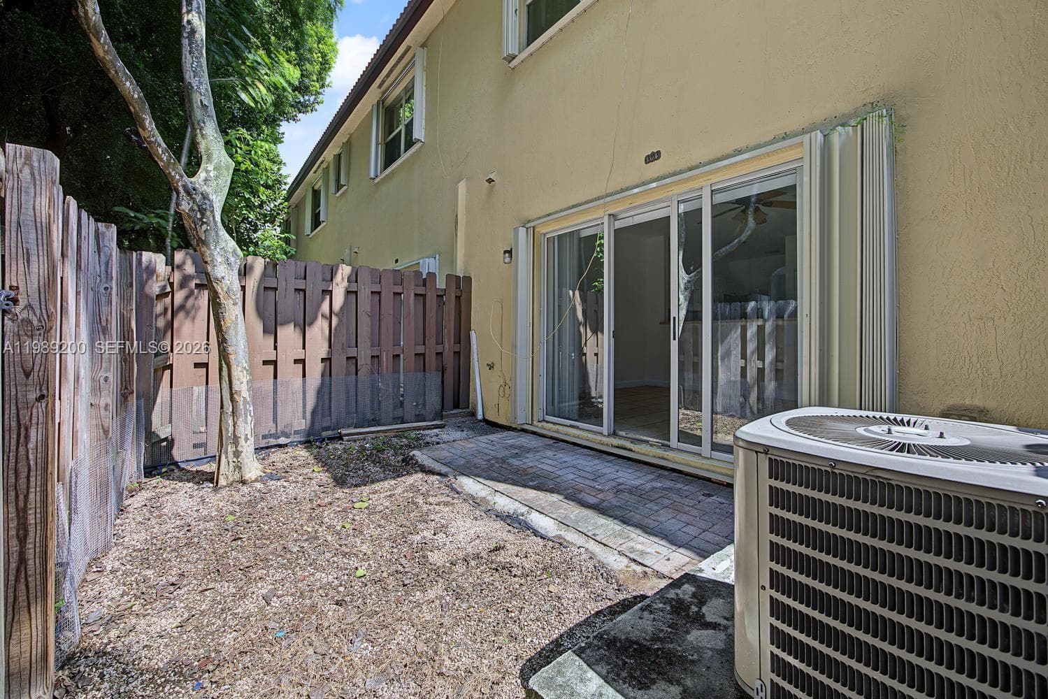 Private patio area with concrete paver flooring, enclosed by vertical wood fencing, featuring large sliding glass doors and exterior HVAC unit