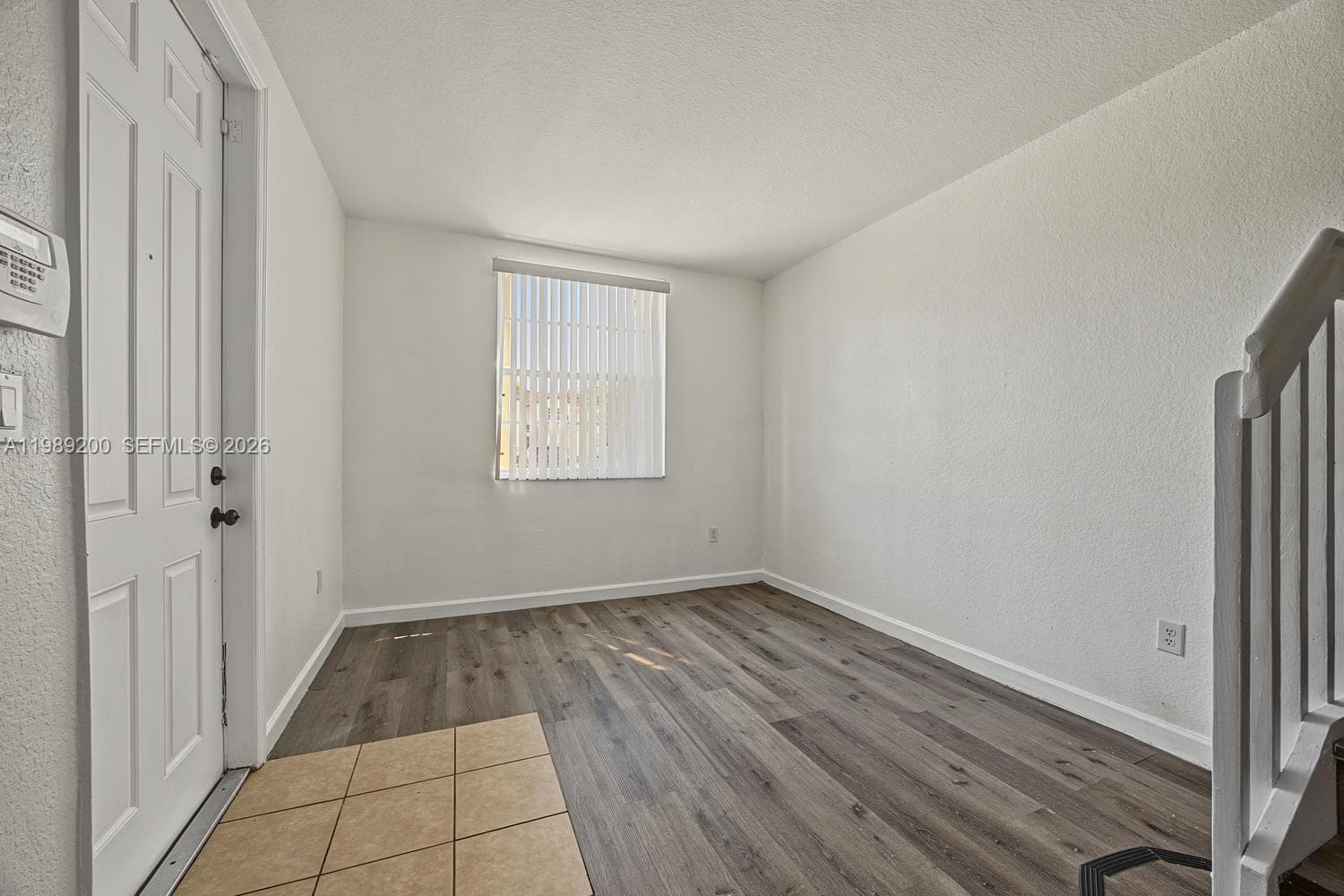 Interior area featuring wood-finish flooring, ceramic tile entryway, vertical window blinds, and white panel door