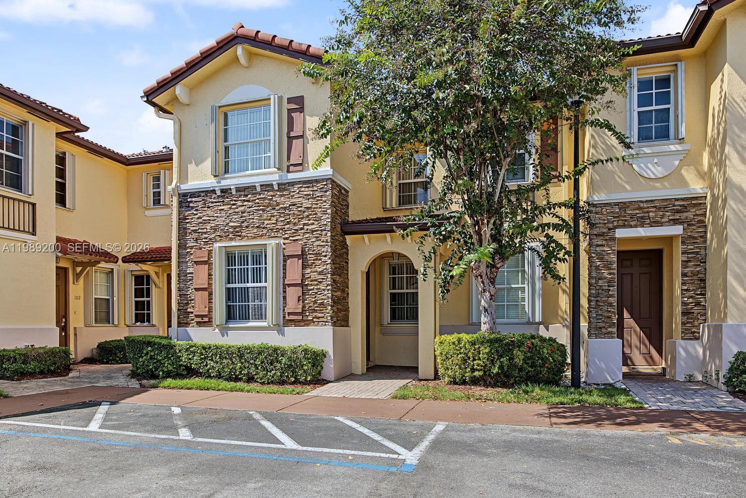 Exterior facade featuring a combination of stucco and stone veneer, mission-style tile roof, decorative shutters, and arched entryway