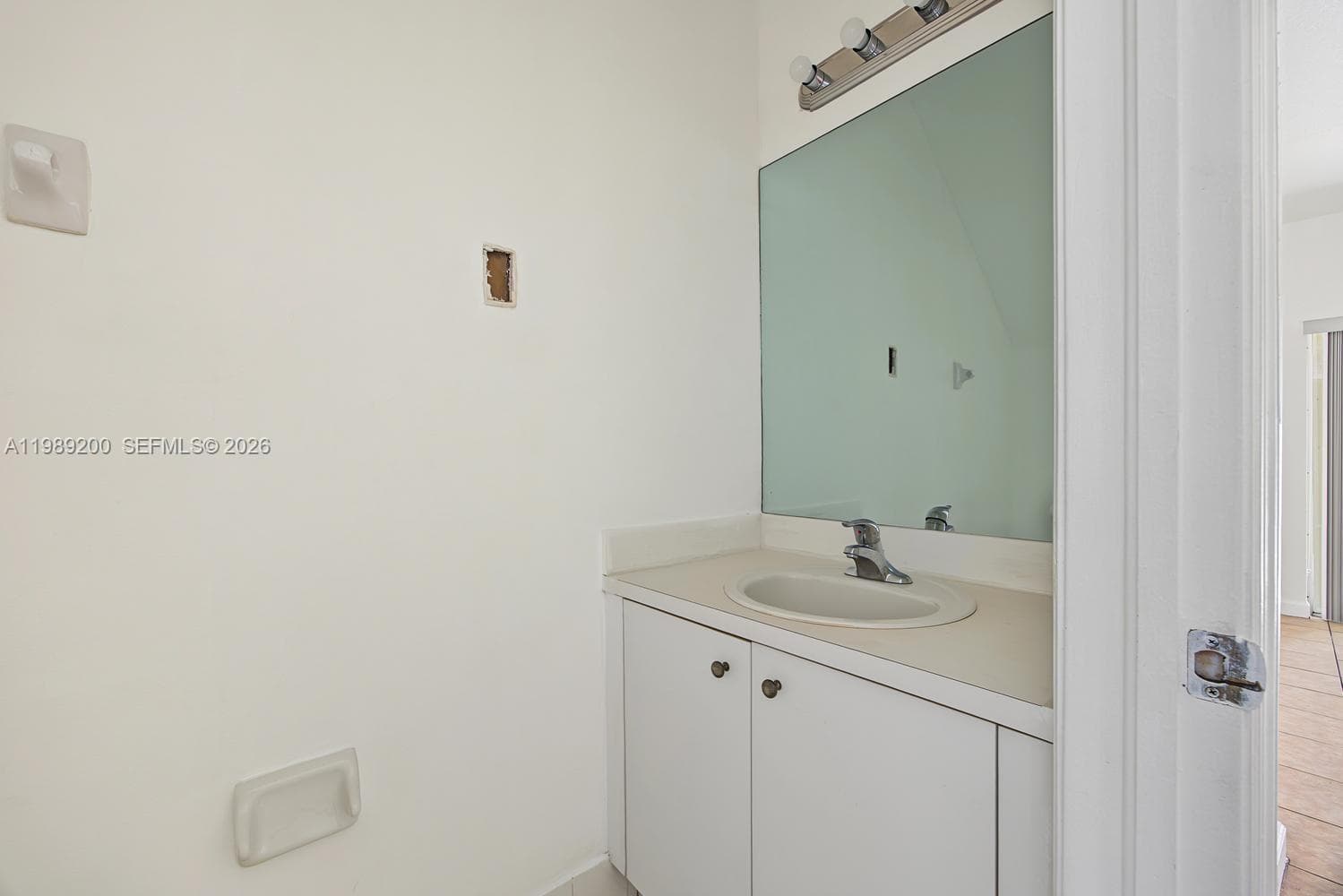 Vanity featuring a white cabinetry base, integrated countertop with an oval drop-in sink, chrome faucet, large rectangular wall-mounted mirror, and overhead tri-light fixture