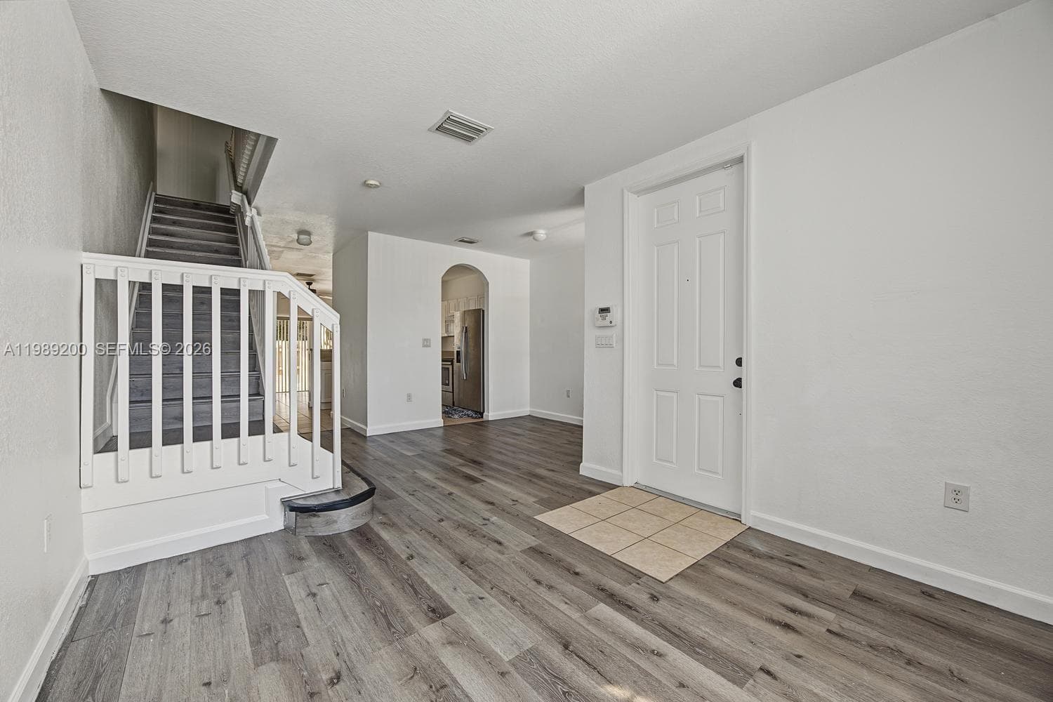 Entryway featuring wood-finish flooring, a six-panel exterior door, ceramic tile inlay at the threshold, an arched interior pass-through, and a staircase with a white railing