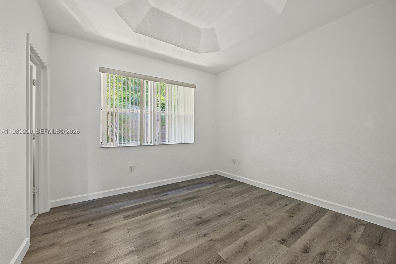 Room featuring wood-finish flooring, a tray ceiling, and a window with vertical blinds