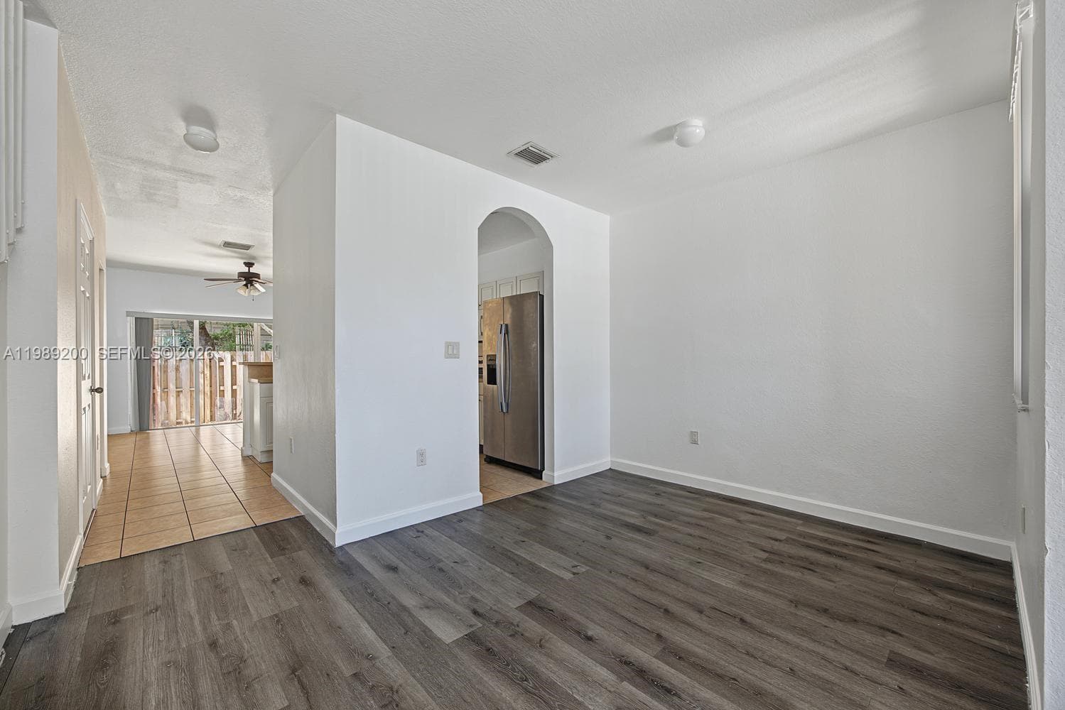 Interior space featuring wood-finish flooring, a neutral color palette, an arched entryway, and tile flooring within the additional room segment