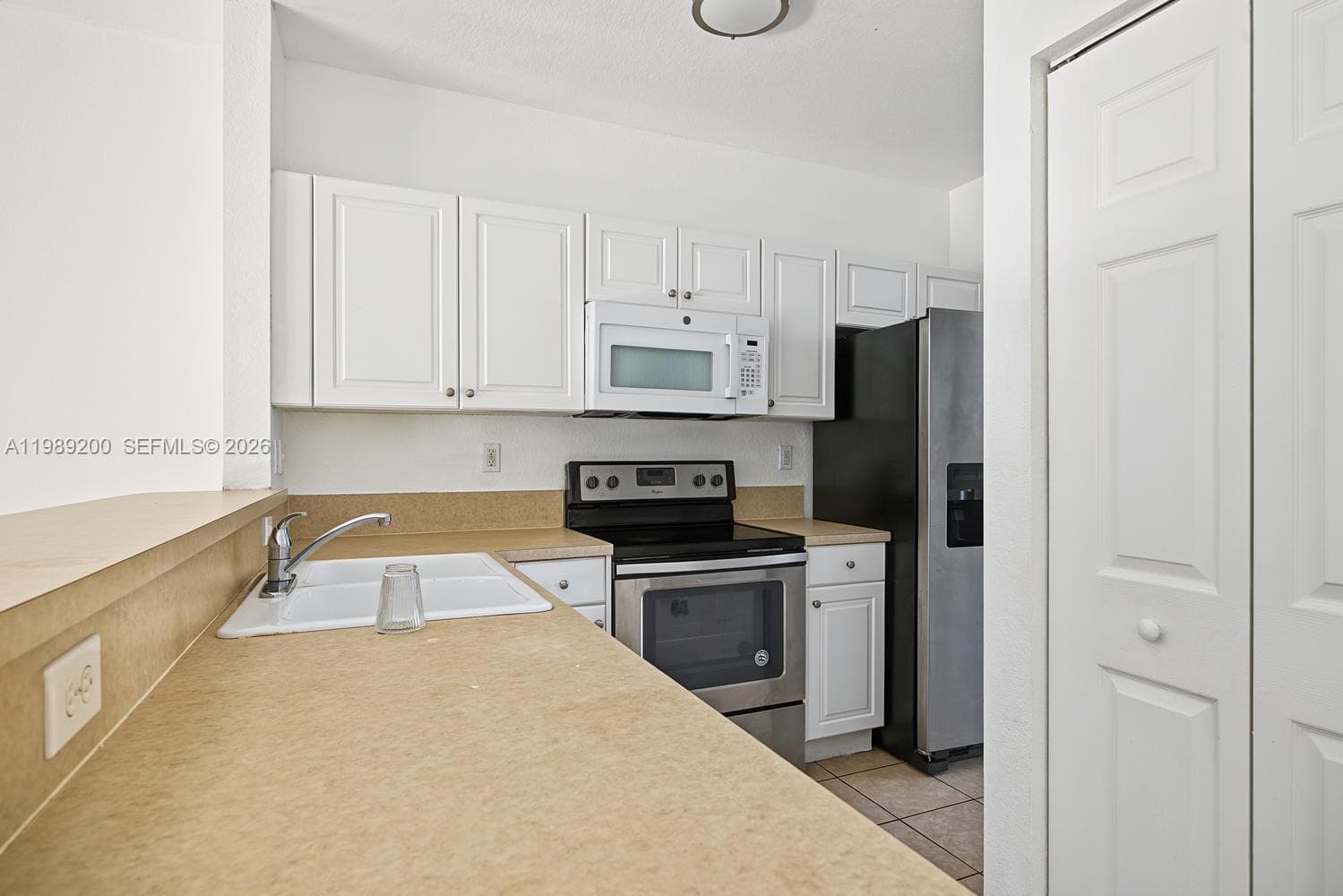 Kitchen featuring white cabinetry, neutral-toned countertops, a dual-basin sink with a gooseneck faucet, stainless steel appliances, and a bi-fold closet door