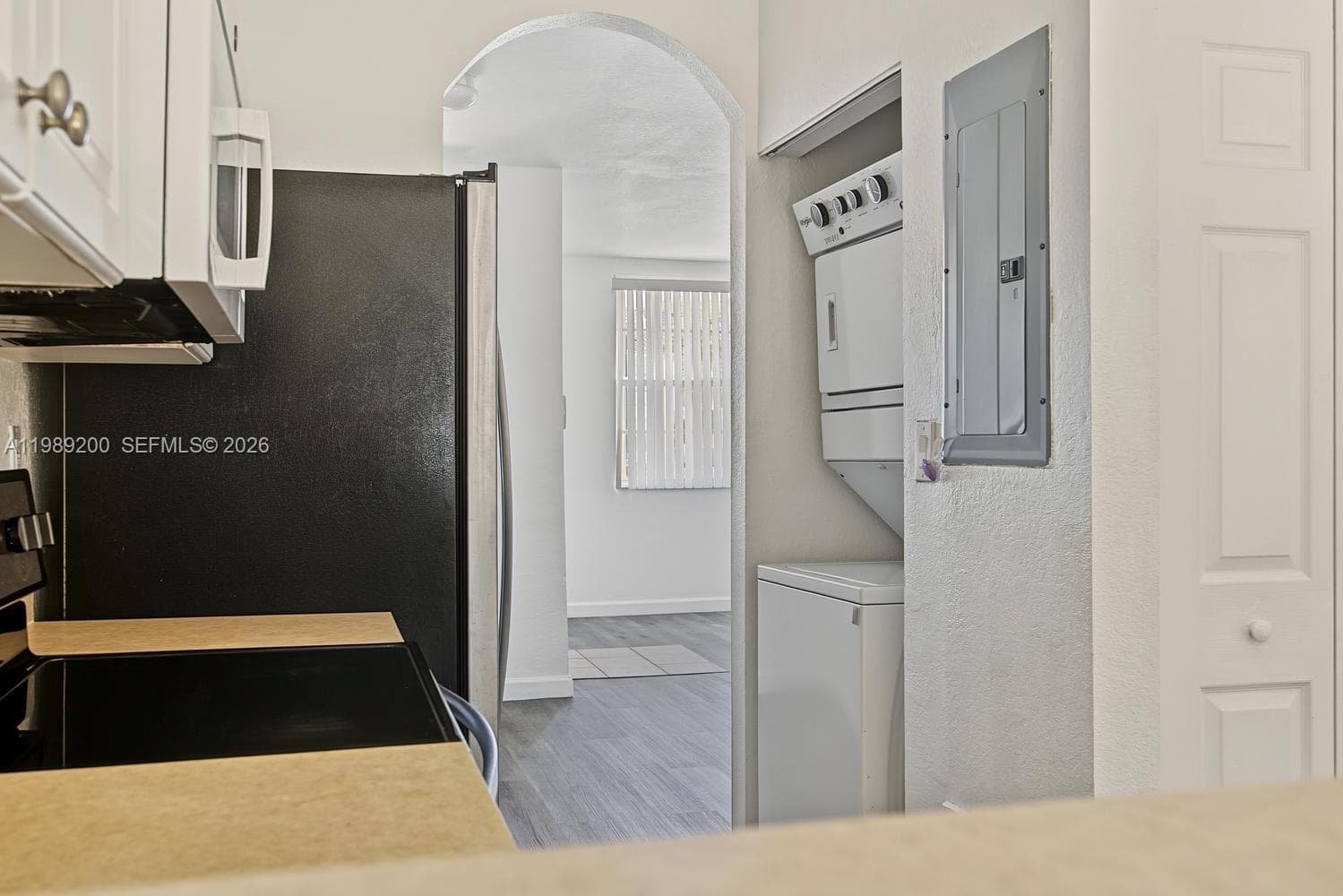 Kitchen featuring light-toned countertops, white cabinetry, a black refrigerator, stacked laundry unit, and a prominent arched entryway