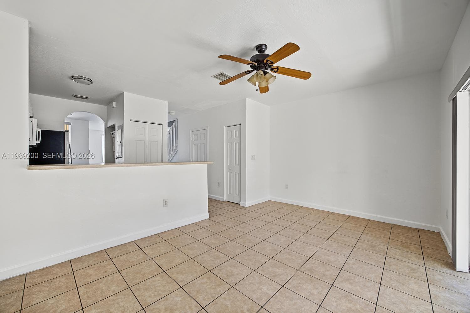 Open-concept space featuring tile flooring, a half-wall partition, a ceiling fan with integrated light fixture, and arched doorway