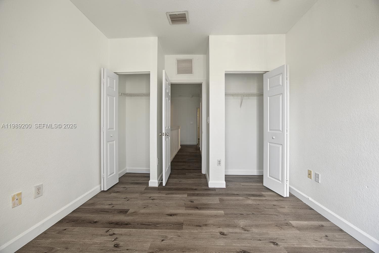 Interior space featuring wood-finish flooring, two closets with white panel doors, and neutral wall tones