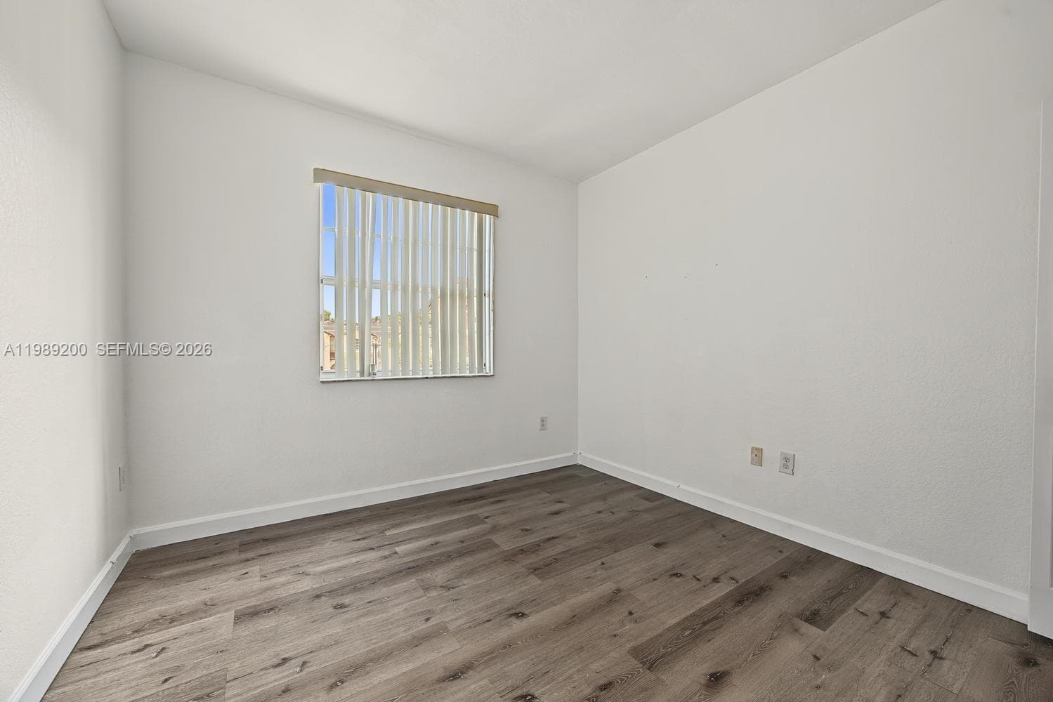 Neutral-toned walls and wood-finish flooring featuring a single window with vertical blinds
