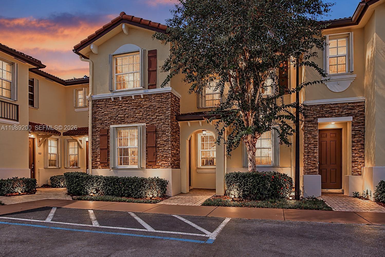 Multi-level stucco exterior featuring stone veneer accents, clay tile roofing, decorative window shutters, and arched entryways