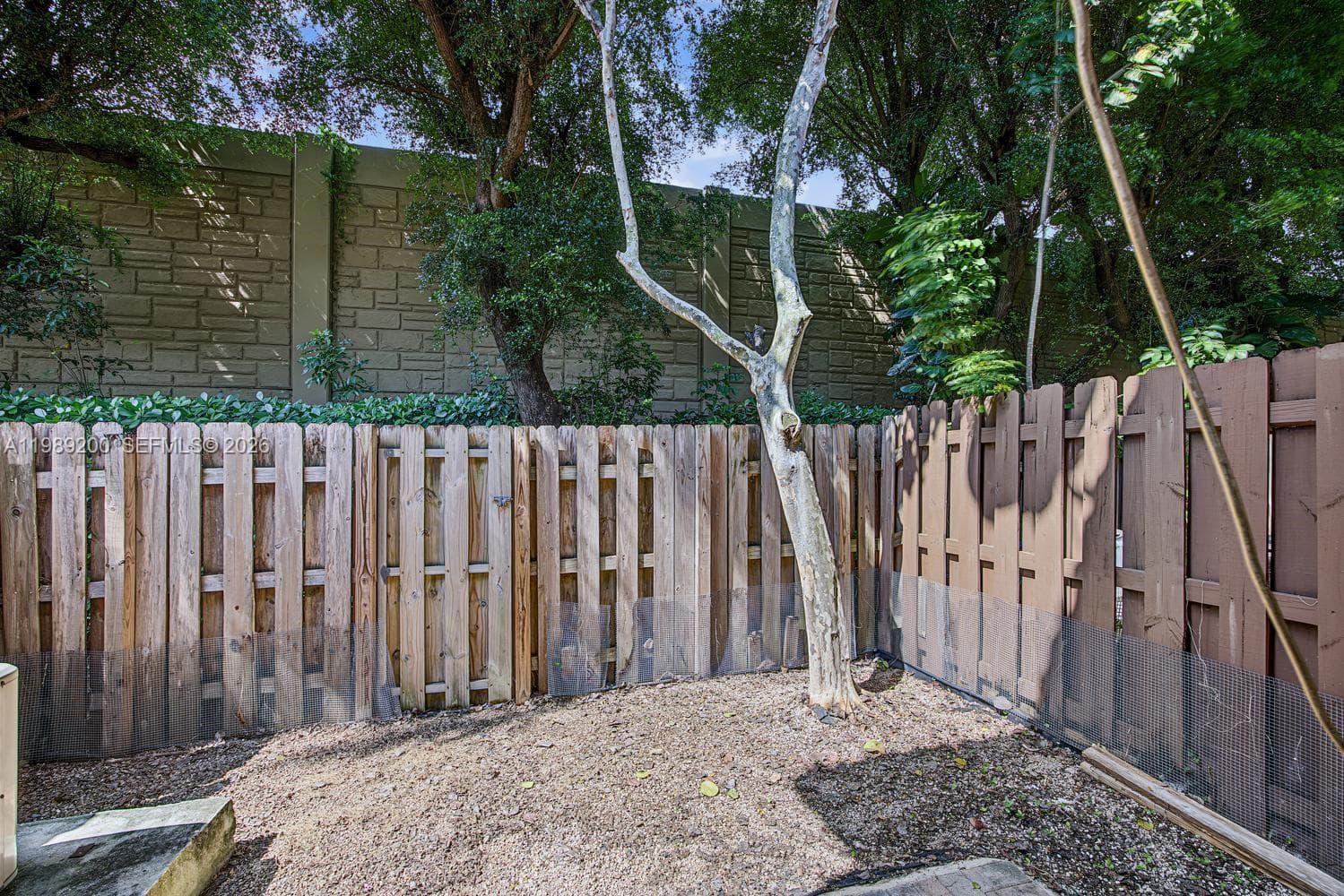Outdoor space featuring a tall textured stone privacy wall, wood-panel fencing, mature trees, and ground-level plantings