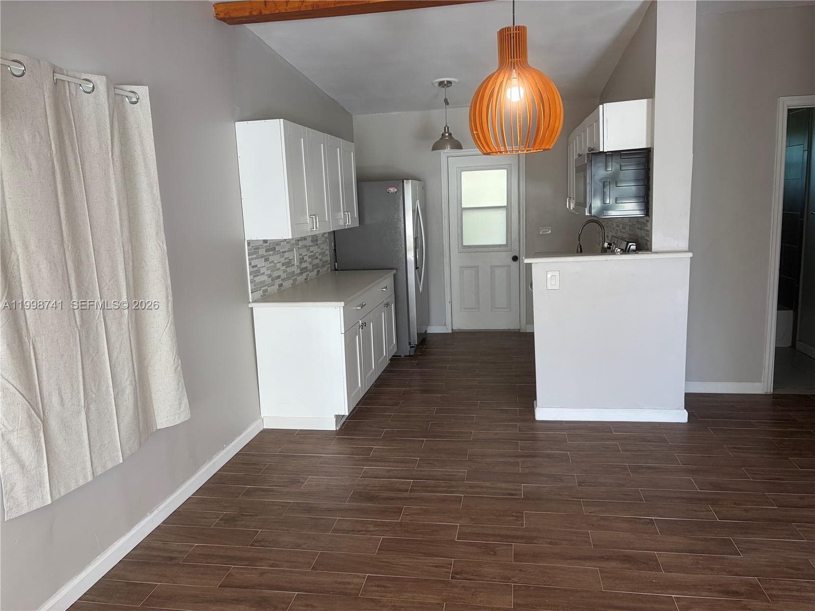 Kitchen featuring white cabinetry, wood-finish tile flooring, a mosaic tile backsplash, a neutral stone-surface countertop, and a structural ceiling beam