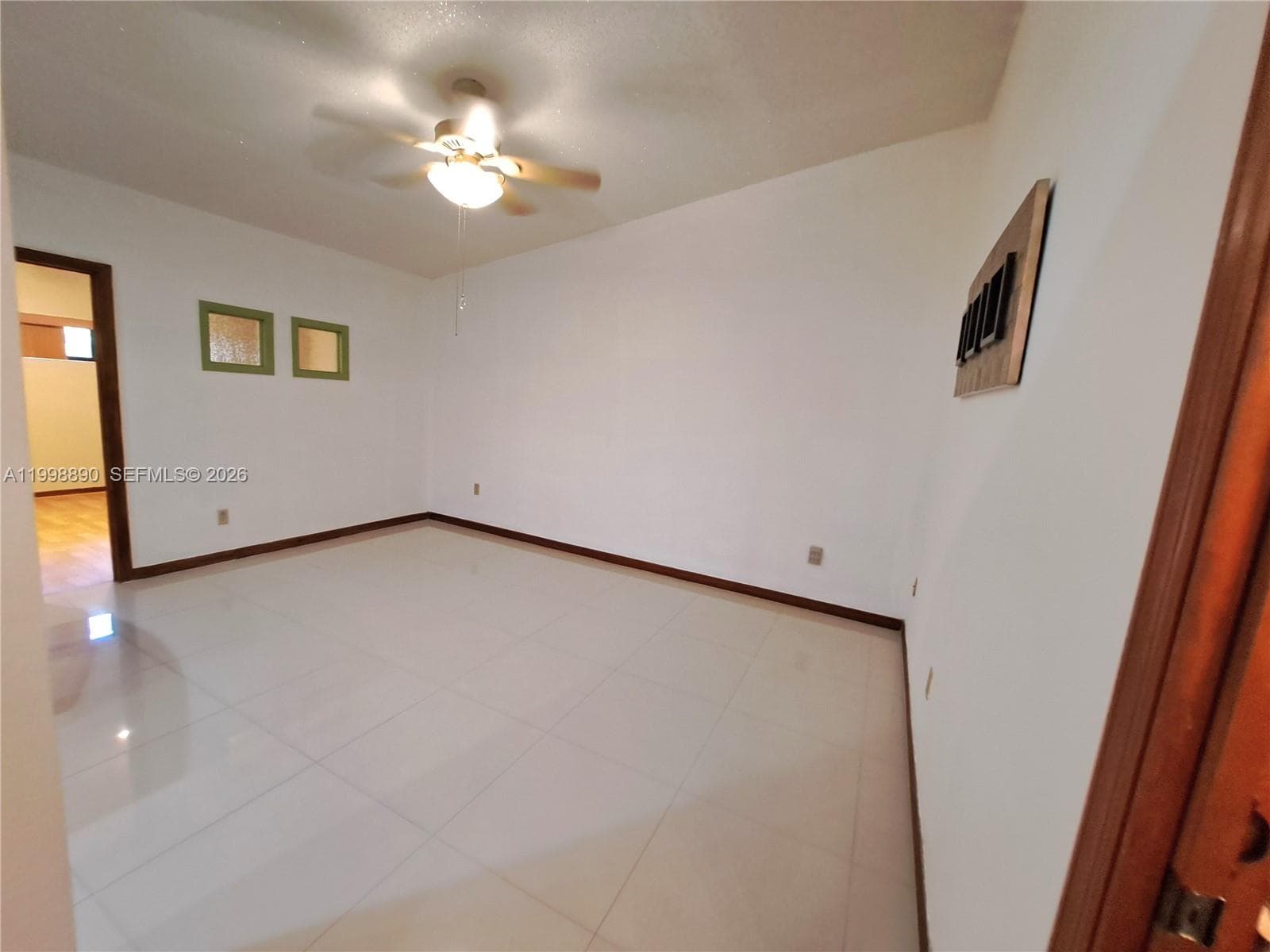 Light-toned tile flooring, neutral walls, ceiling fan with integrated light fixture, and square recessed wall insets with wood-finish trim
