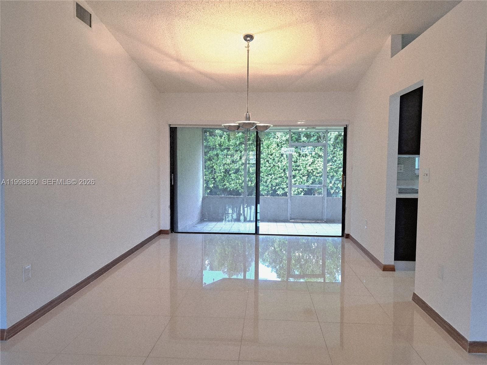Vaulted ceilings, large-format tile flooring, polished metal pendant lighting, and sliding glass doors opening to a screened-in patio area